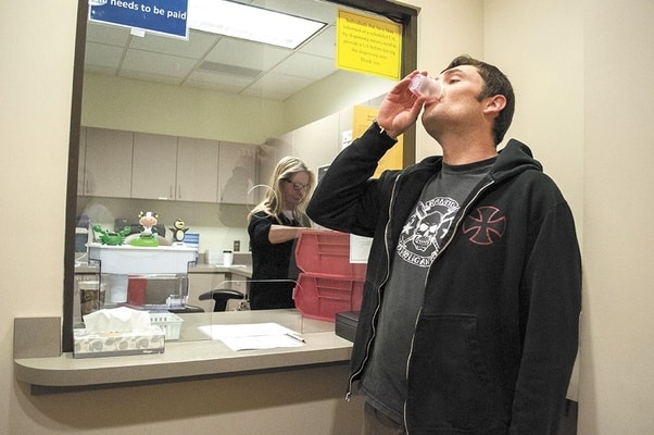 A man drinks his daily dose of methadone for his opiate use disorder at the methadone clinic. He is no longer using heroin and is not at risk of overdose due to his enrollment in a medicated recovery program.