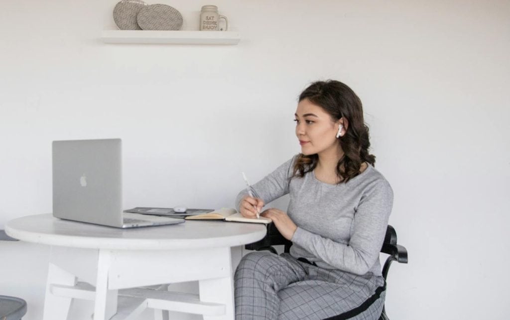 Adult woman studying online for CADC certification North Carolina at a wooden desk with a laptop, notebook, and coffee in soft natural light.